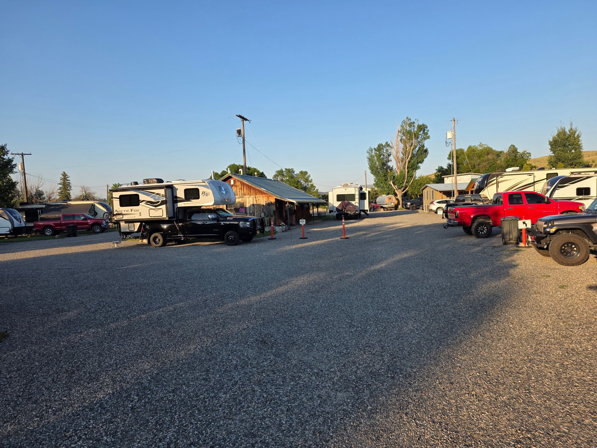 Campground with various RVs and trucks parked on gravel under a clear blue sky.