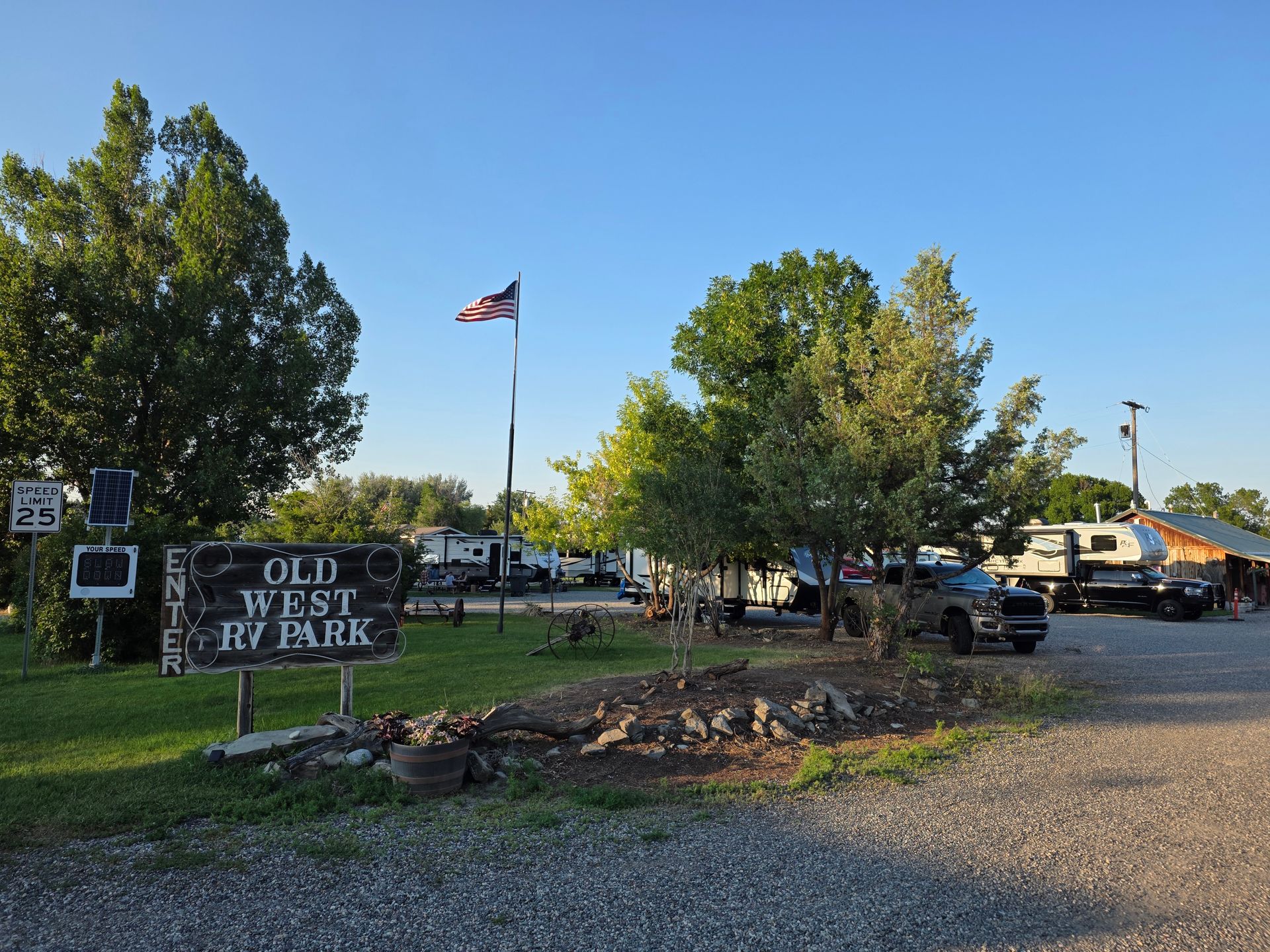 Sign for Old West RV Park with RVs and flag in the background.