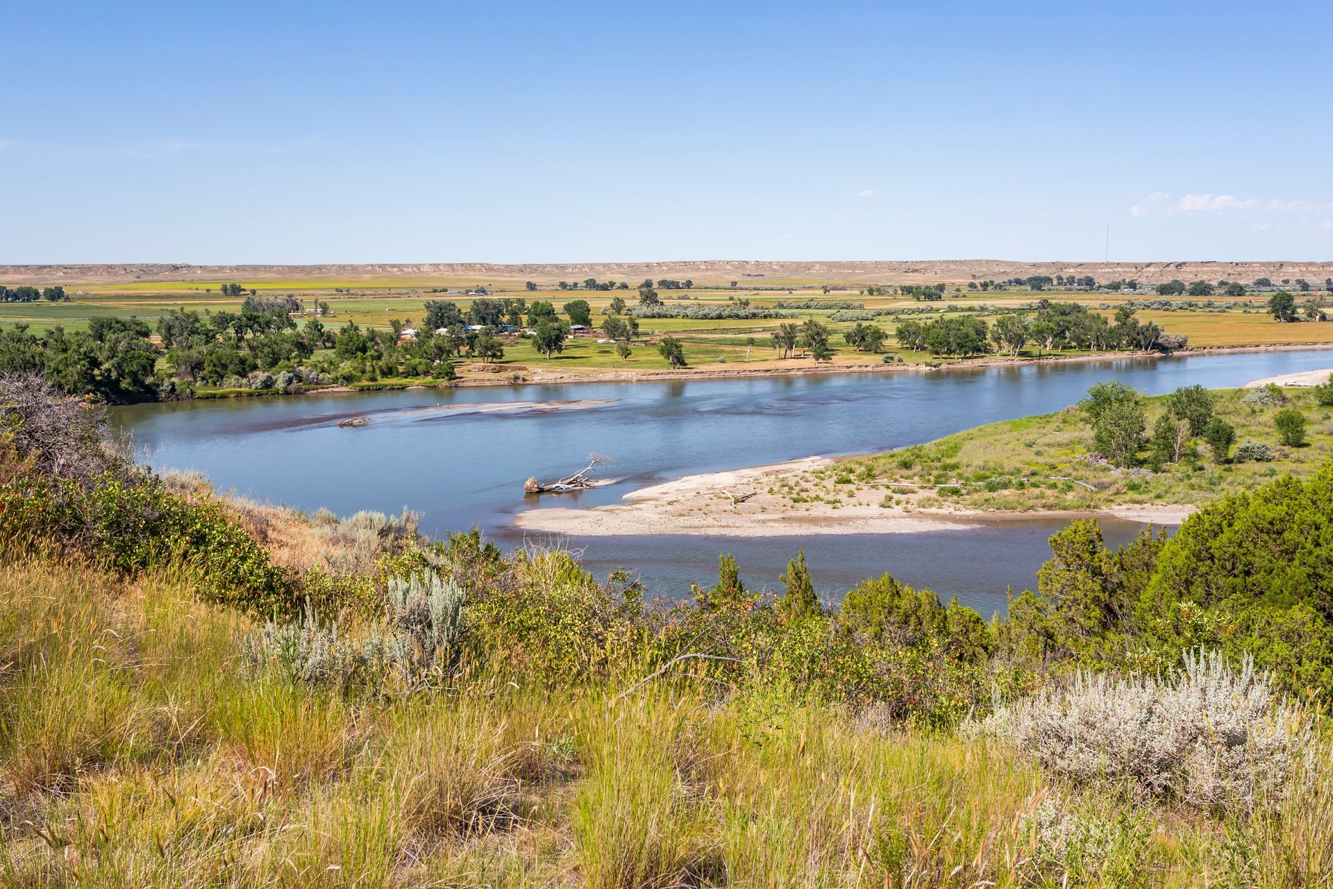 Wide river landscape with blue water, green vegetation, and a clear blue sky.