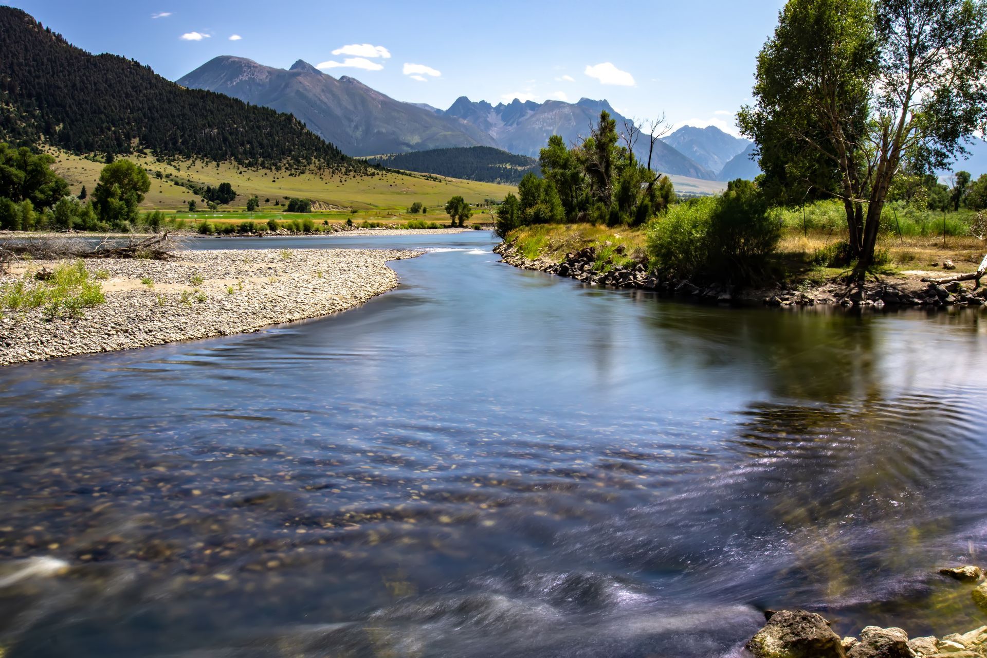 River flowing through a valley with mountains in the background under a sunny sky.