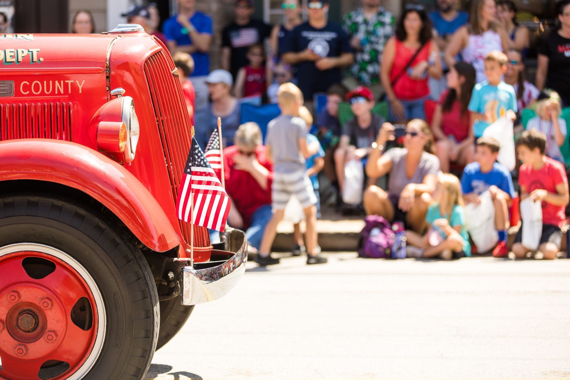 A red fire truck is parked in front of a crowd of people watching a parade.
