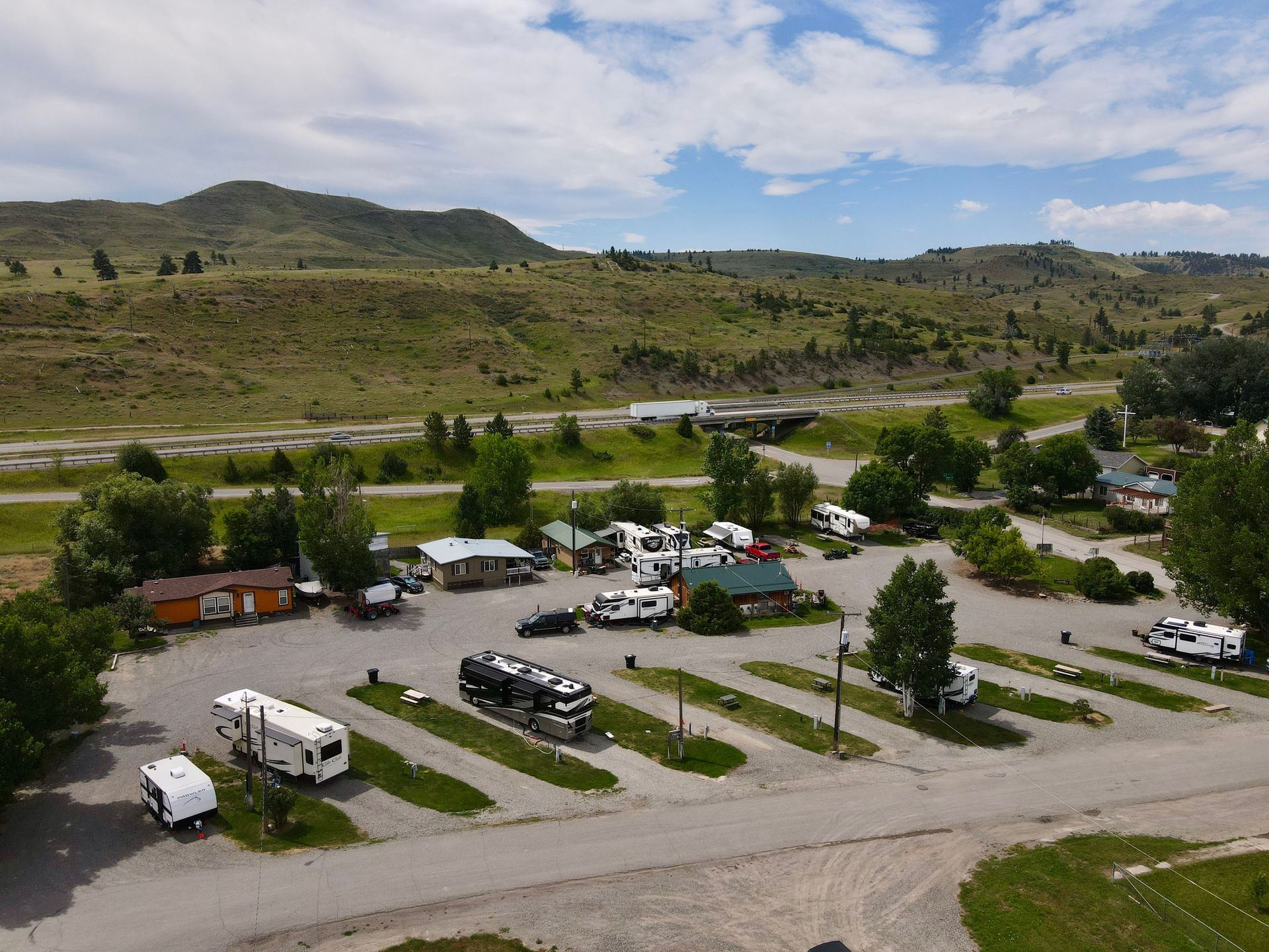 RV park with campers, buildings, and mountains in the background on a partly cloudy day.