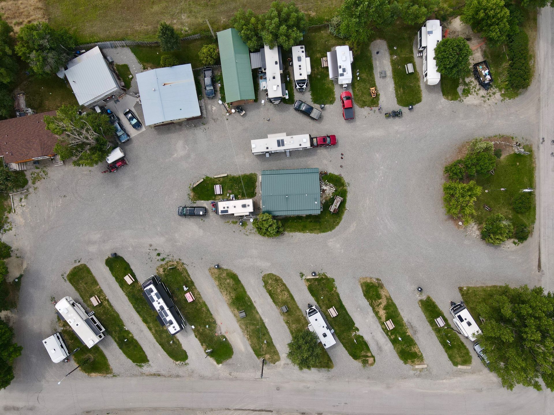 Aerial view of a campground with RVs parked on gravel and grass sites, with trees and buildings.