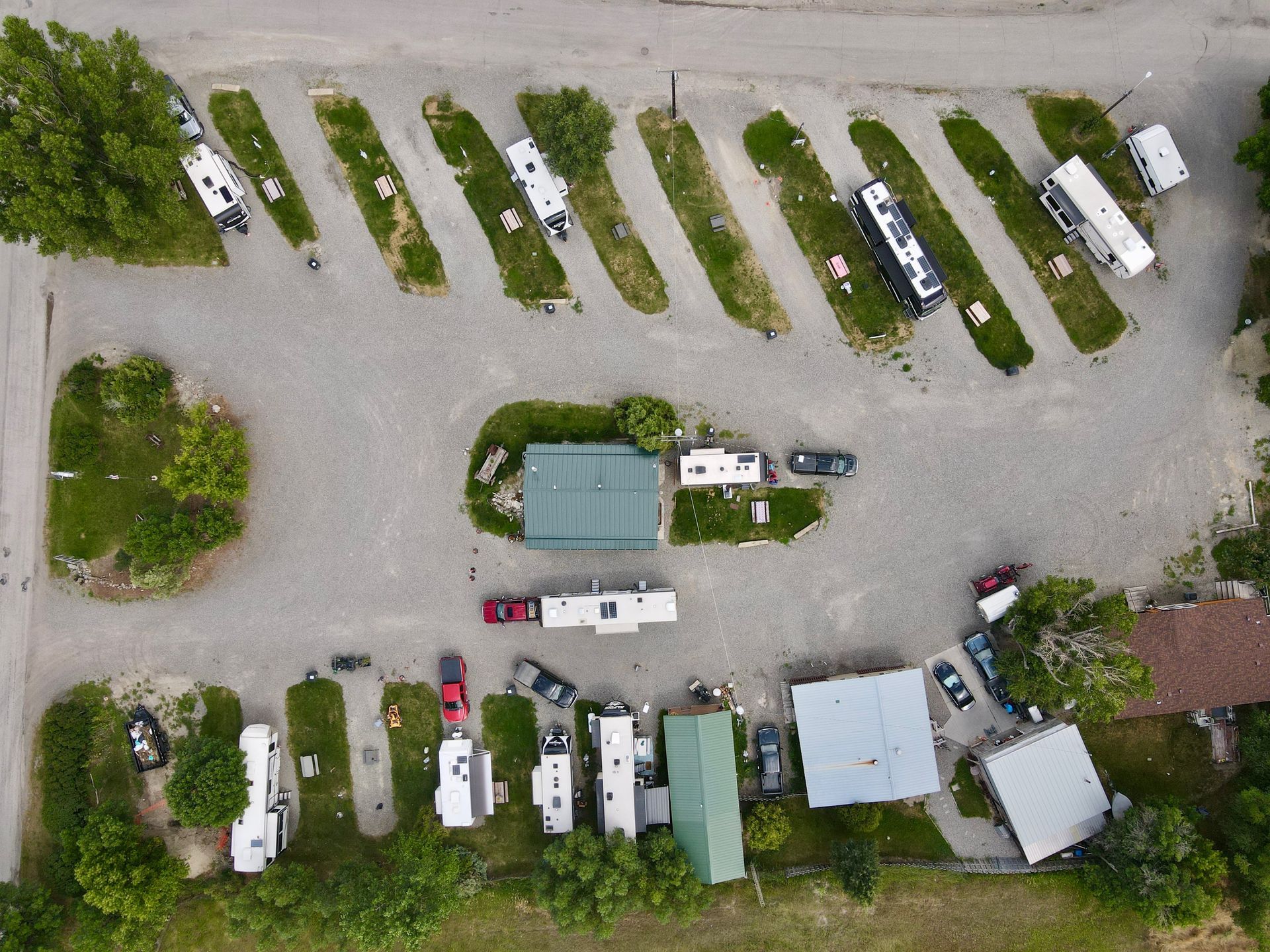 Aerial view of an RV park with parked RVs, gravel lots, green spaces, and buildings.