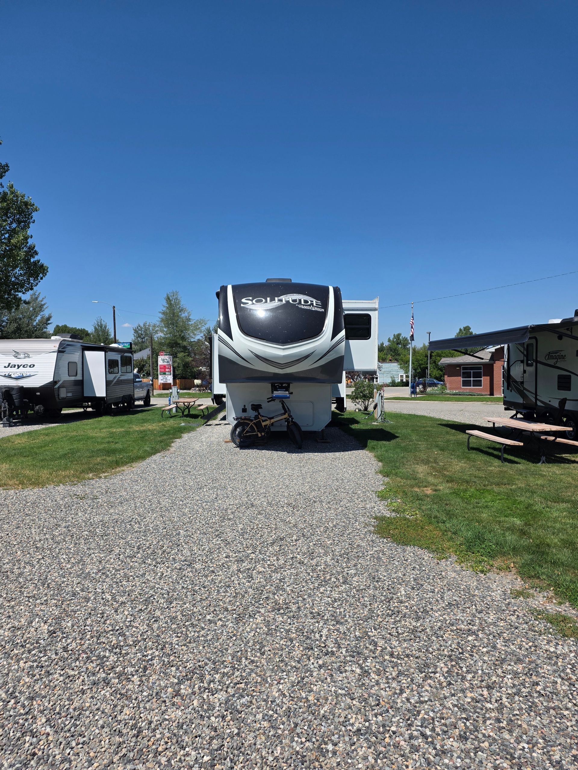 A white and gray fifth-wheel trailer parked on gravel, under a blue sky.