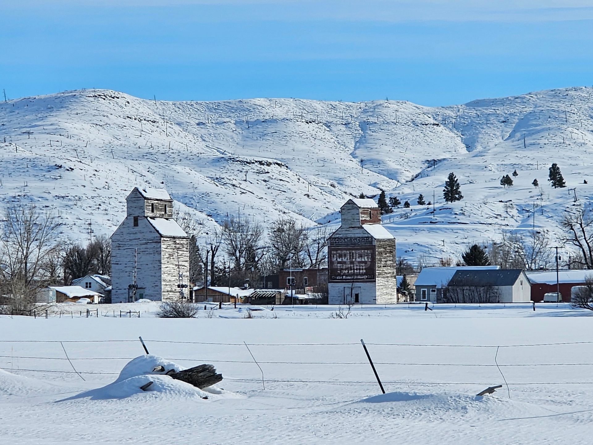 A snowy landscape with a few buildings in the foreground and mountains in the background.
