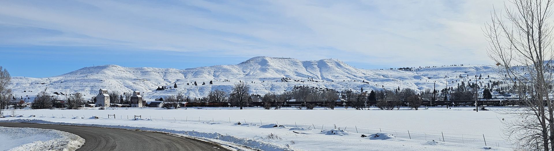 A snowy field with mountains in the background and a road in the foreground.