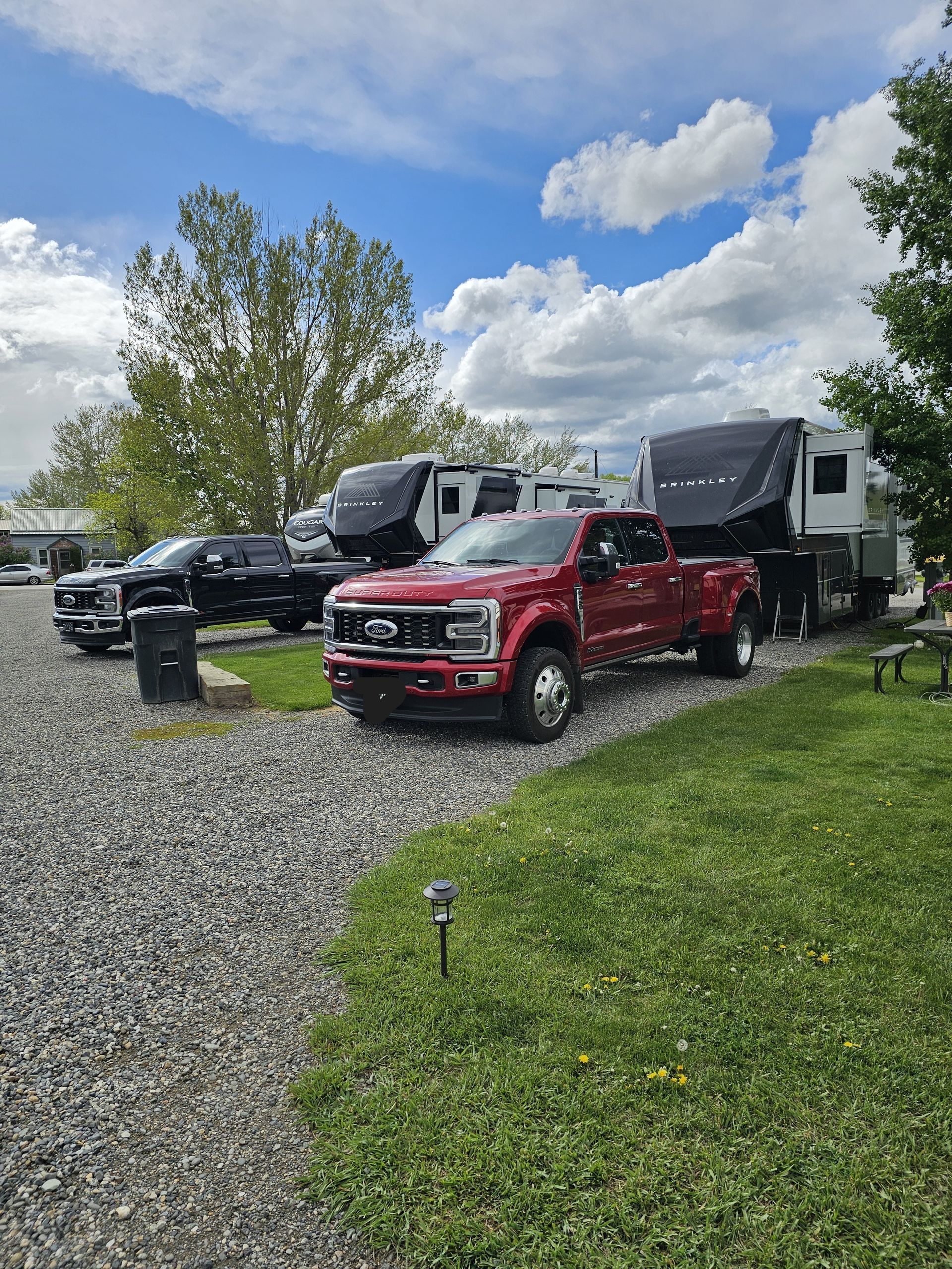 A red truck is parked next to a trailer in a gravel lot.