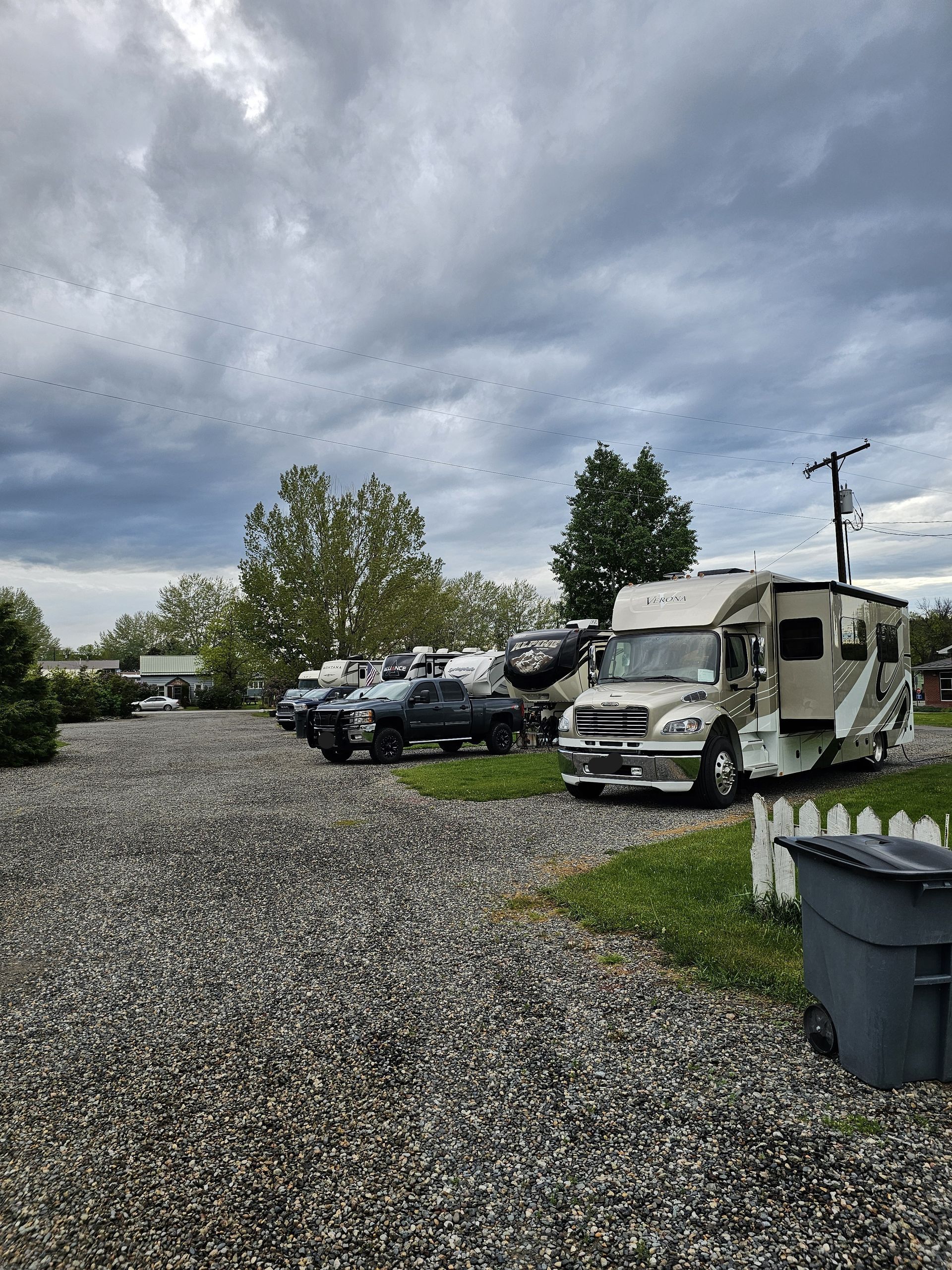 A row of rvs are parked in a gravel lot.