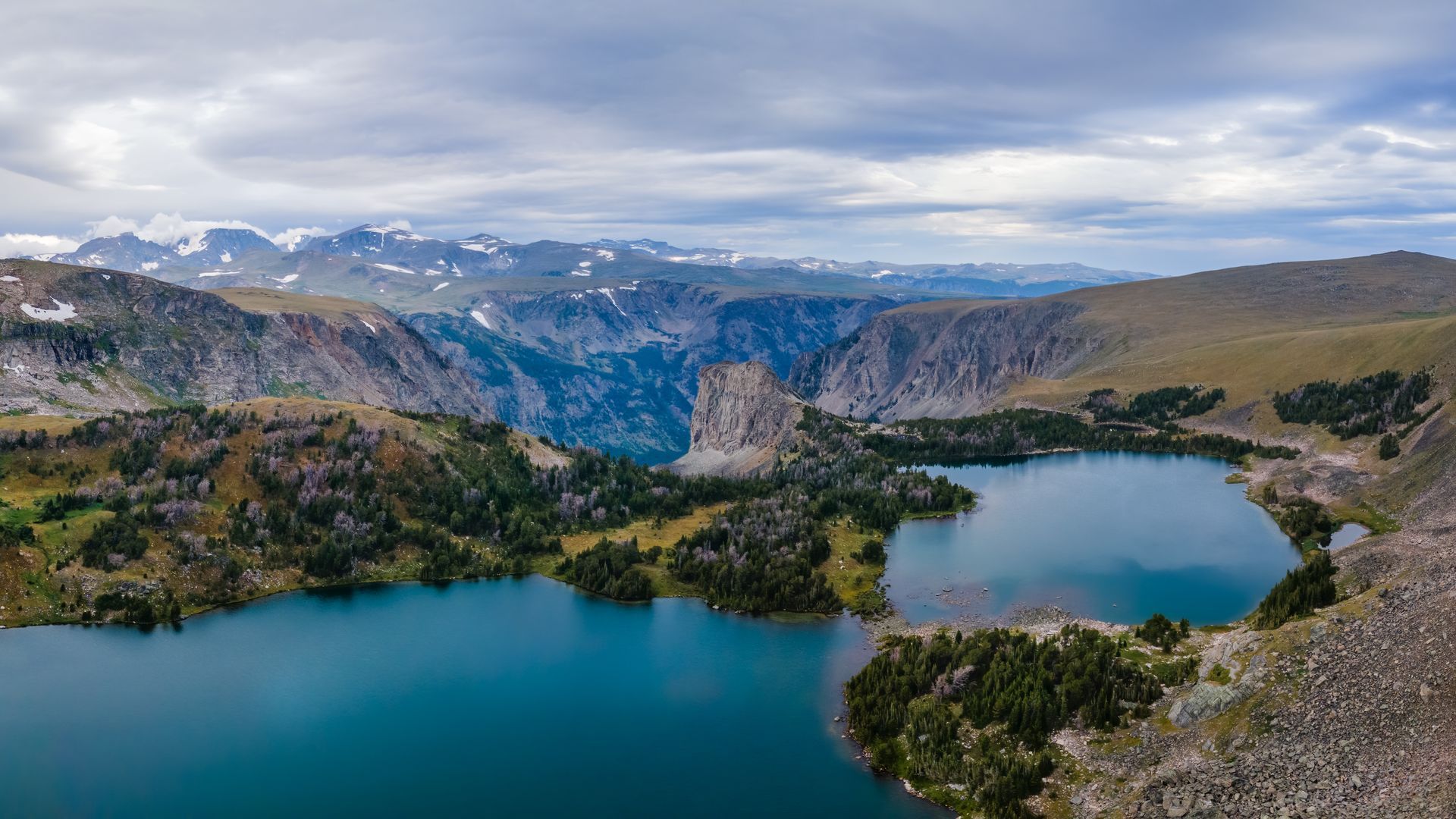 An aerial view of a lake surrounded by mountains on a cloudy day.