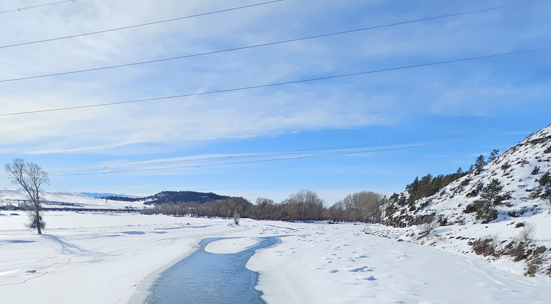 A river runs through a snowy field on a sunny day.