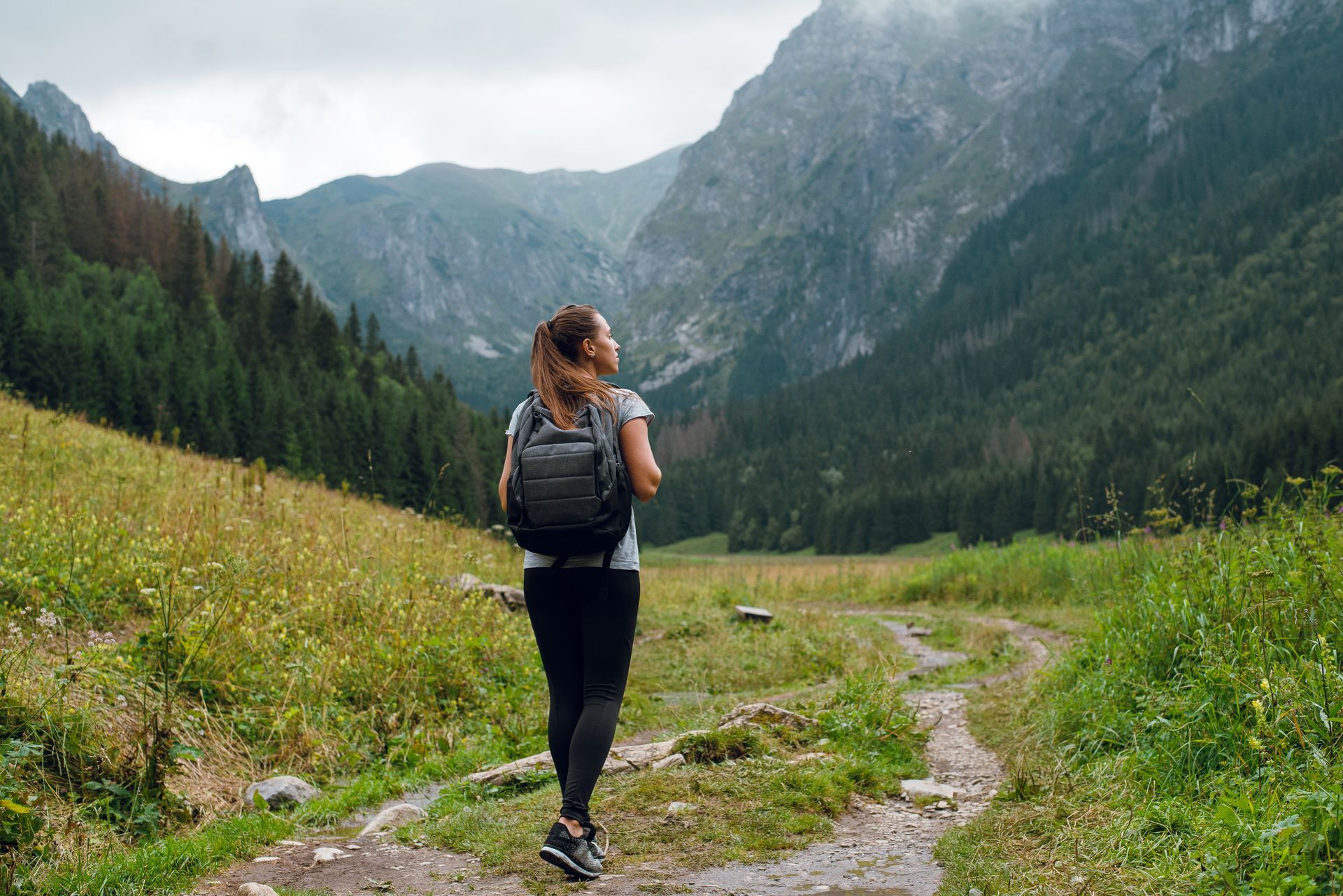 A woman with a backpack is walking down a path in the mountains.