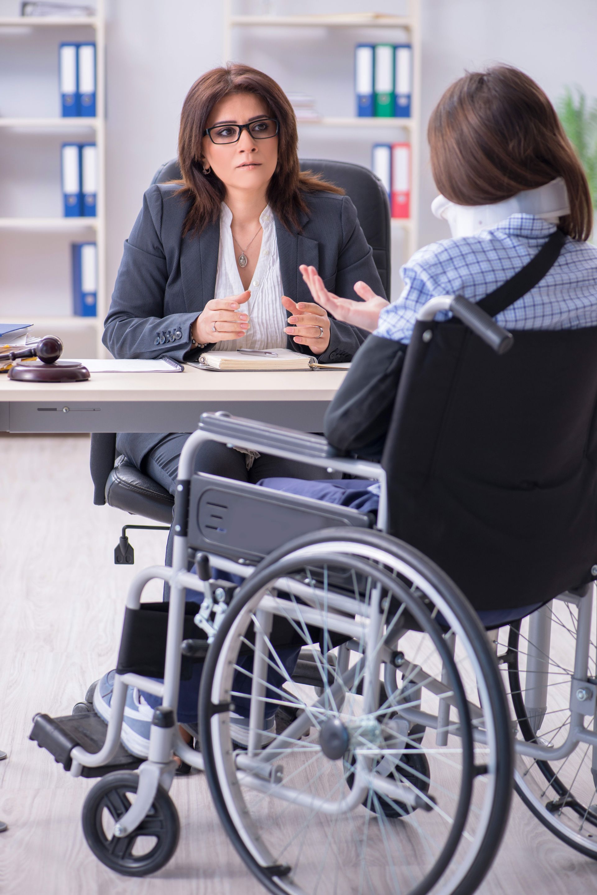 Woman in wheelchair with neck brace talking to a lawyer in an office setting.