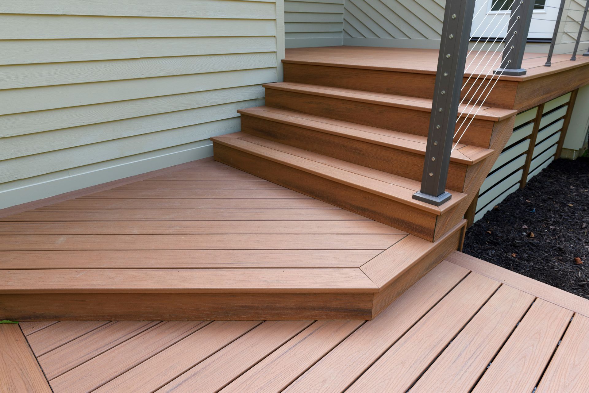 Wooden deck with stairs leading to a higher level. Brown deck boards with a modern cable railing.