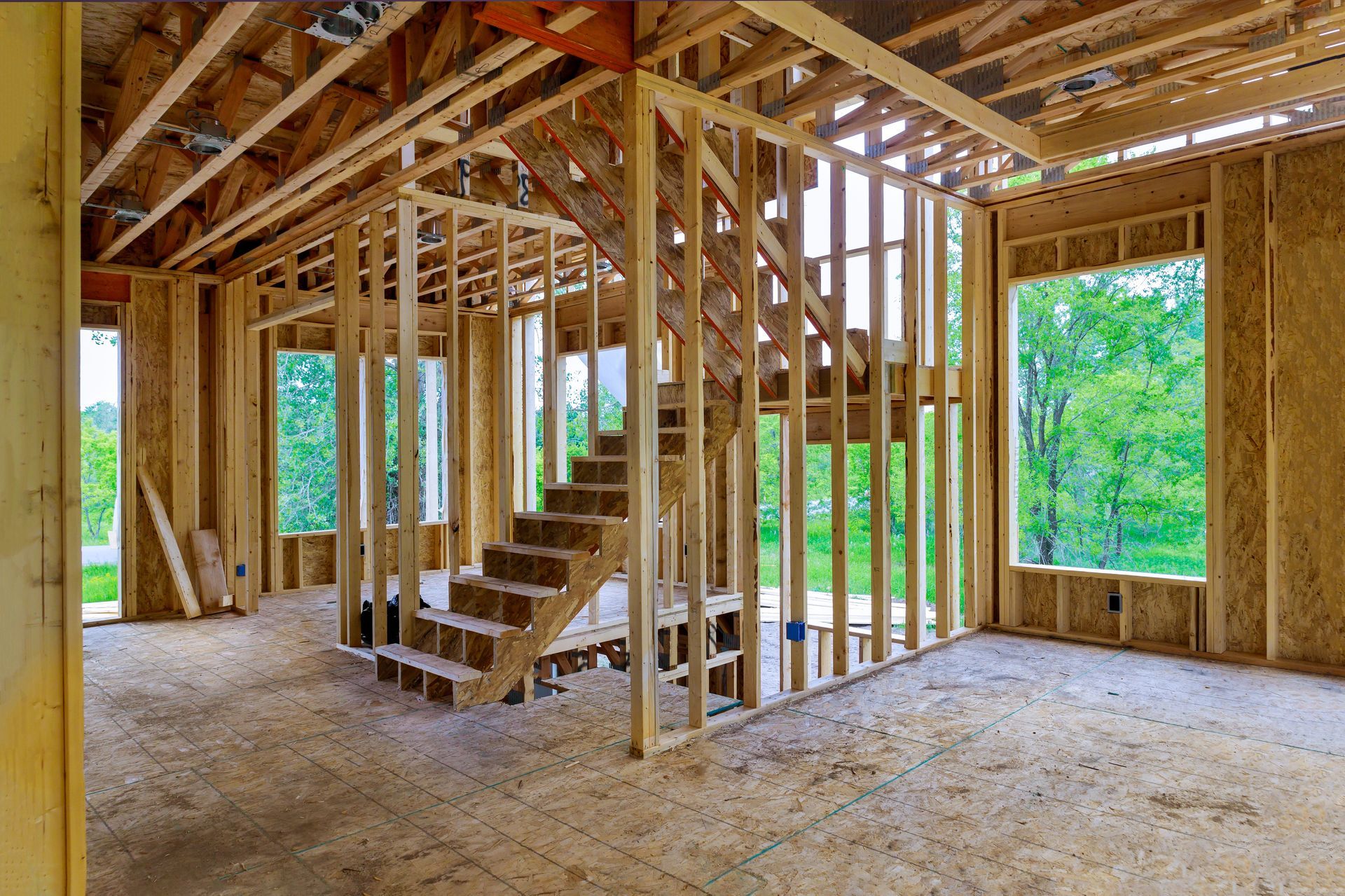 Wooden frame construction of a house interior with staircase and windows.
