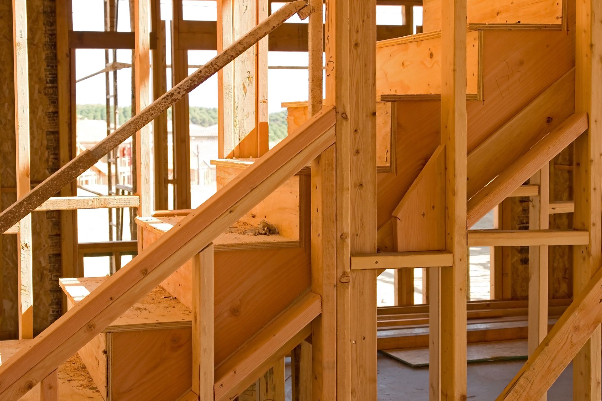 Wooden staircase under construction inside a building, with handrails, supports, and open framing.