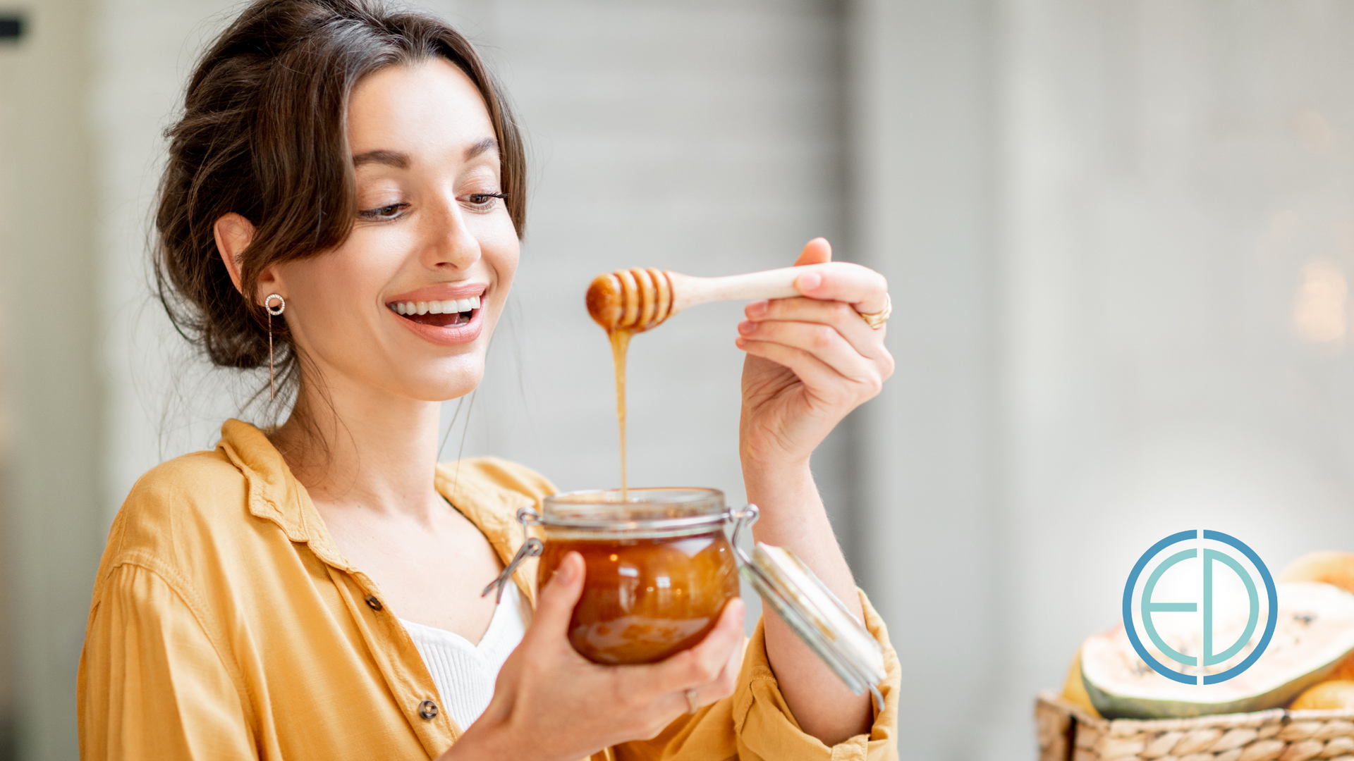 Woman smiles, holding honey jar and dipper, kitchen setting, light colors.