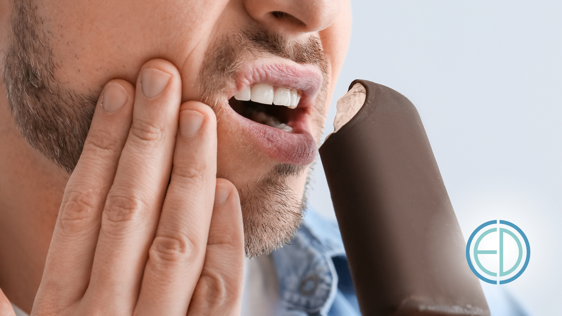 A man is eating an ice cream bar and has a toothache.