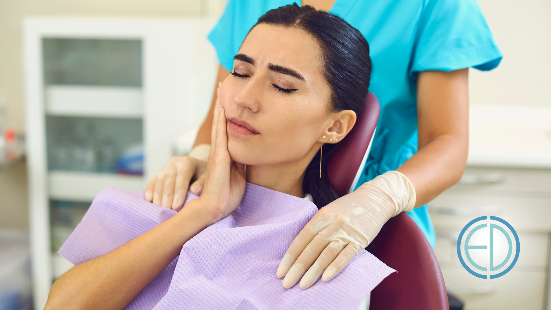 Woman in dental chair with hand on cheek, showing pain, dentist in background.