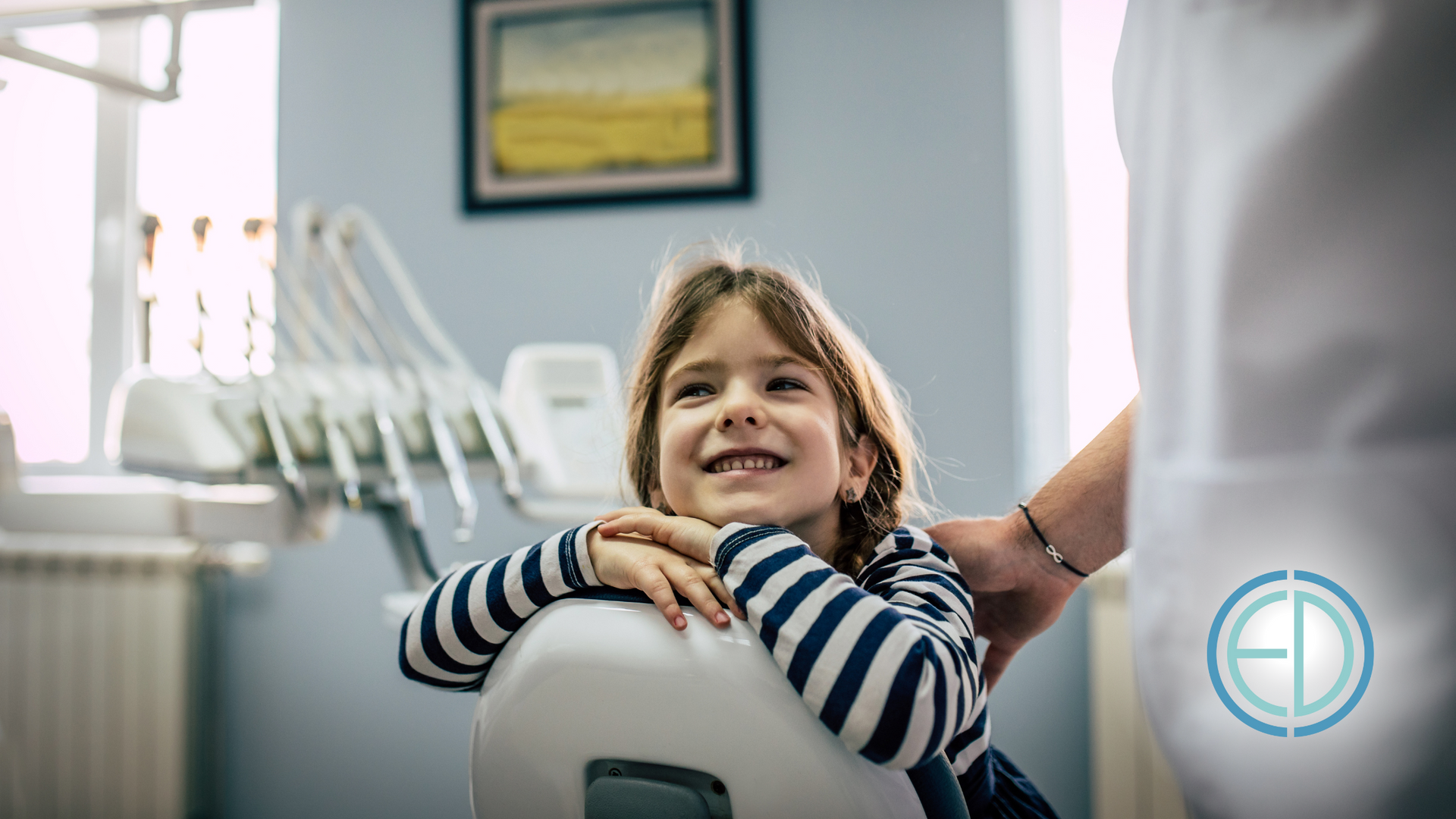 A little girl is sitting in a dental chair and smiling.