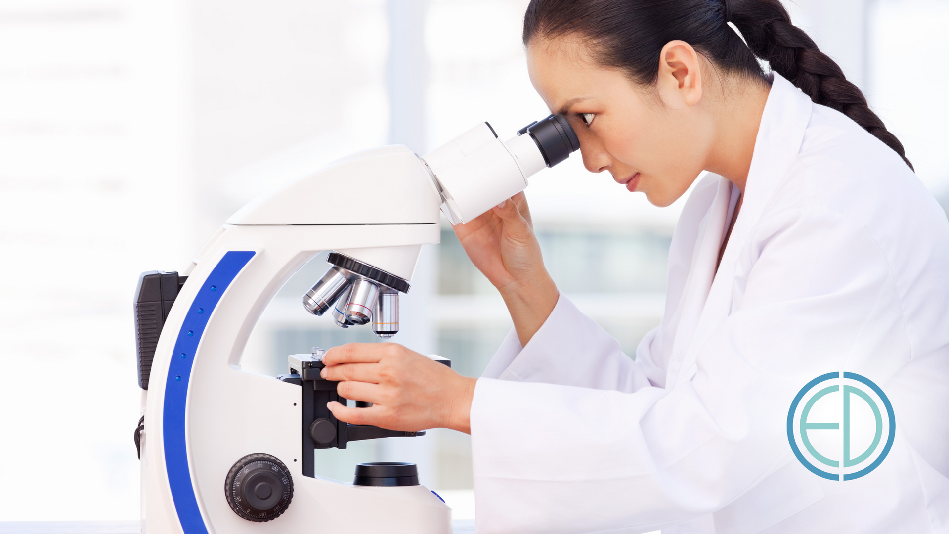 A woman in a lab coat is looking through a microscope.