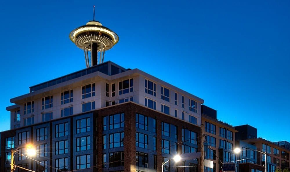 Exterior view of a modern apartment building at dusk with the Space Needle in Seattle in the background.