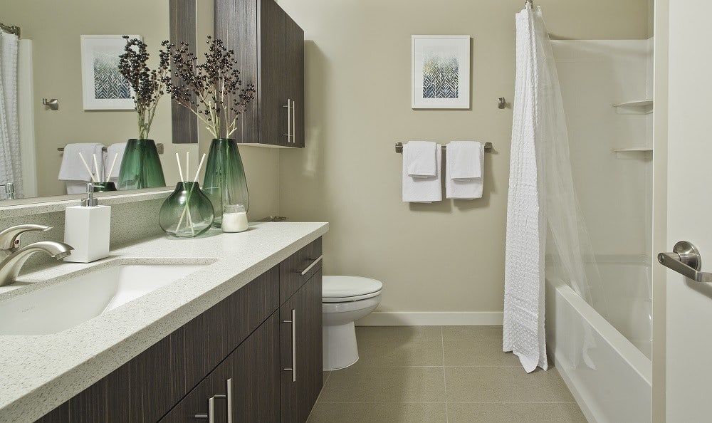 Bathroom with a long vanity, sink, toilet, and a tub/shower in neutral tones.