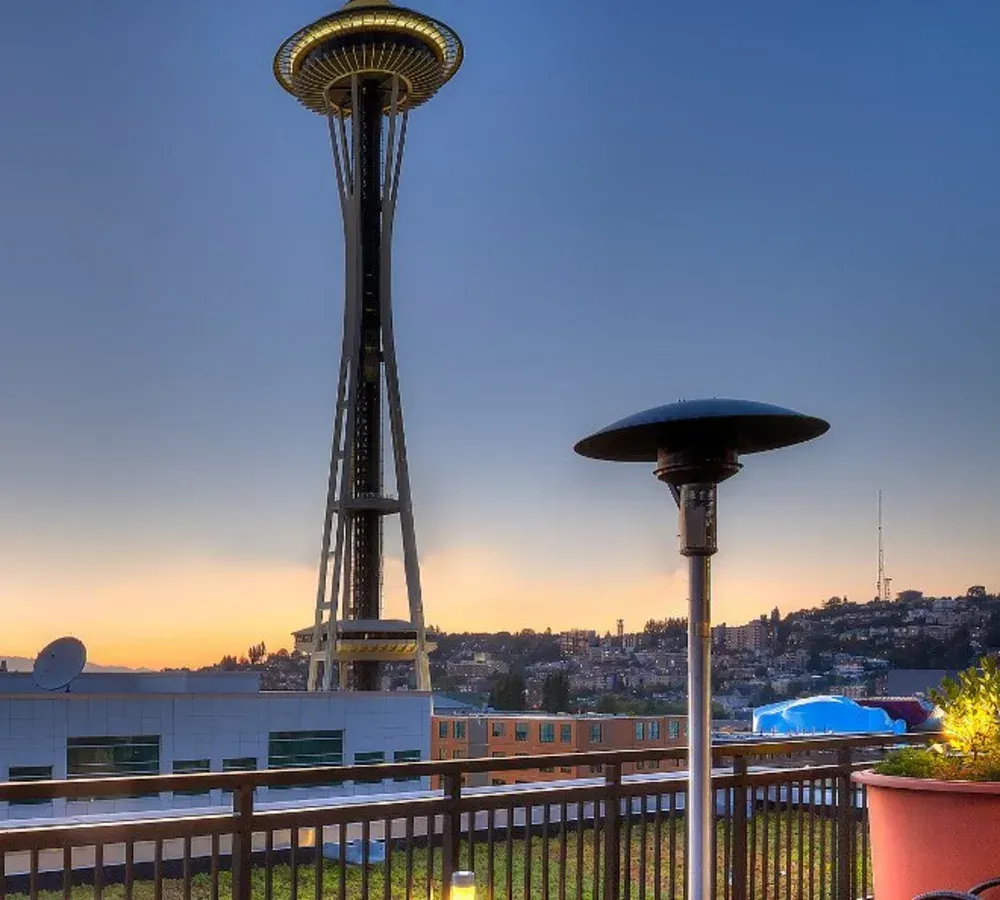 Rooftop terrace with a heater and railing overlooking the city skyline at sunset.