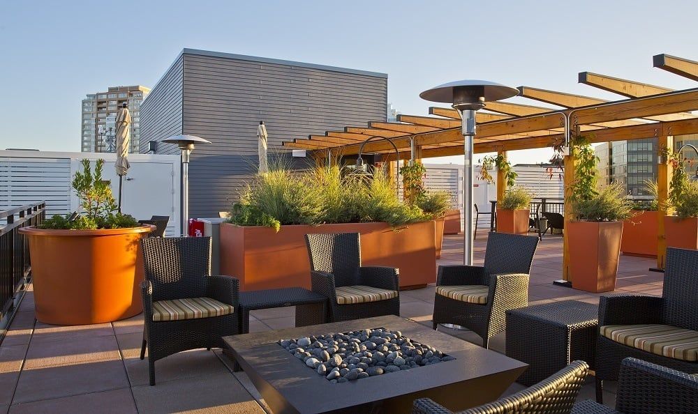 Rooftop terrace with wicker seating, large planters, and a central fire pit.