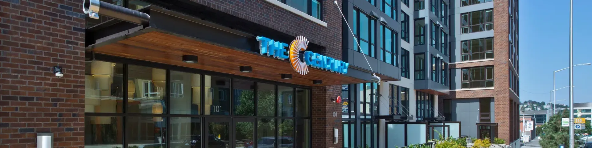 Exterior view of The Century apartment building entrance with brick facade and glass doors.