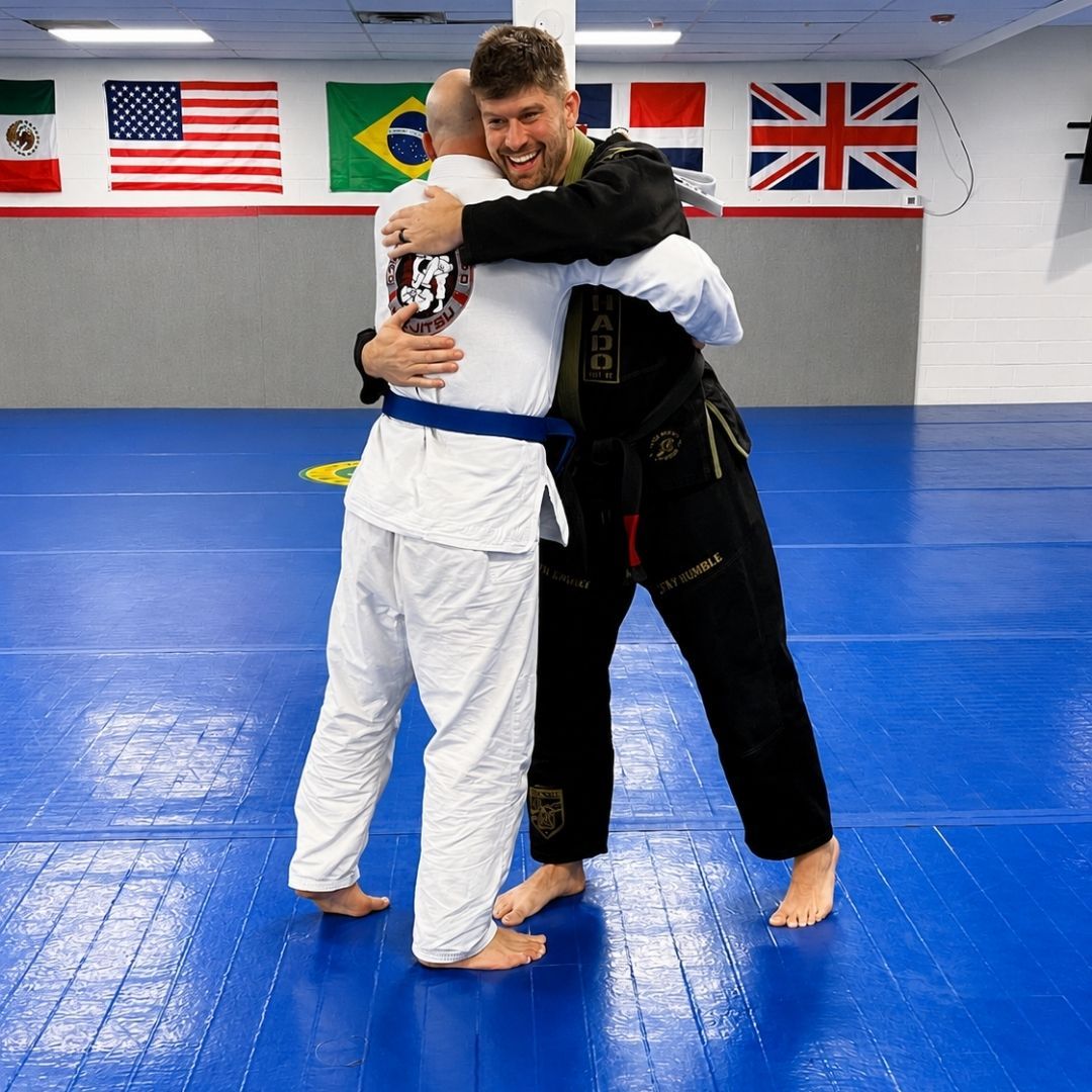 Two people practicing Brazilian Jiu-Jitsu on a mat; one in a black gi, one in a white gi, grappling.