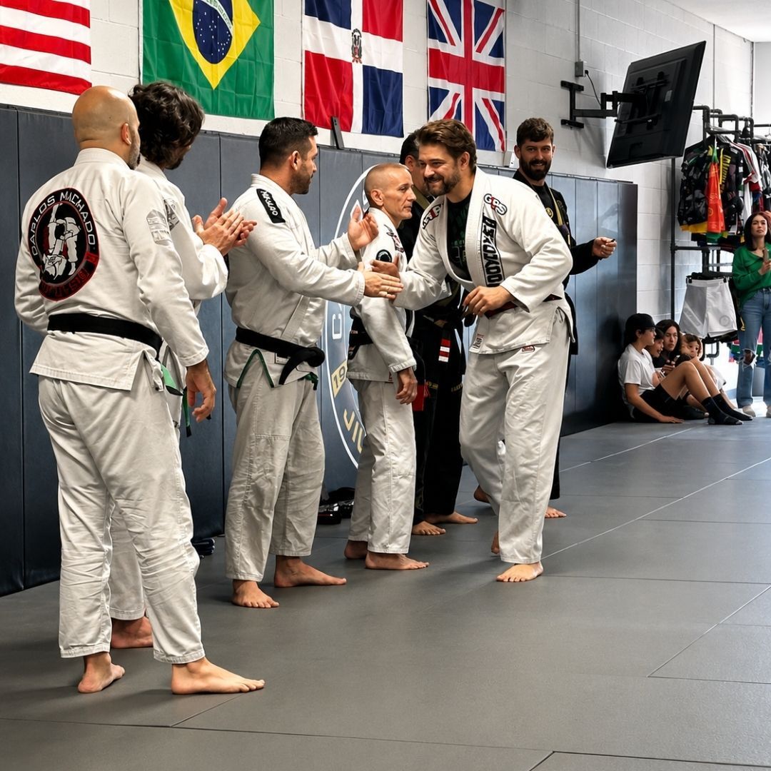 Five people in jiu-jitsu gear pose together in a gym.  Smiling,  some have arms around each other. Machado logo visible.