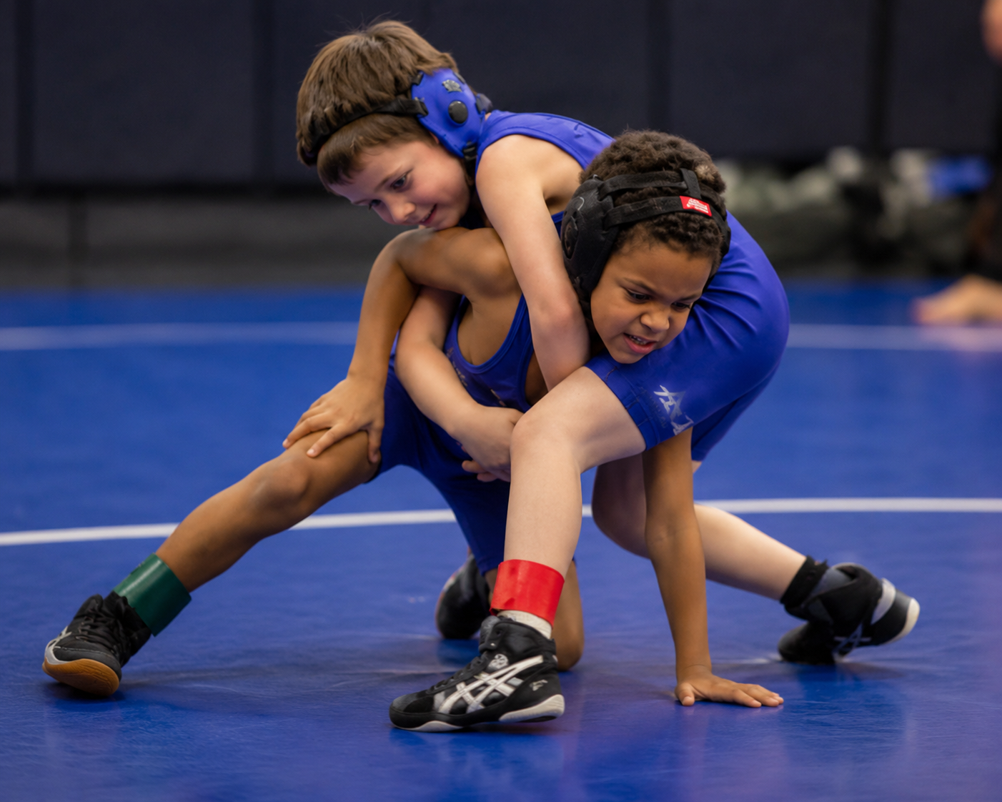 Two children grappling on a mat, one in a headlock.