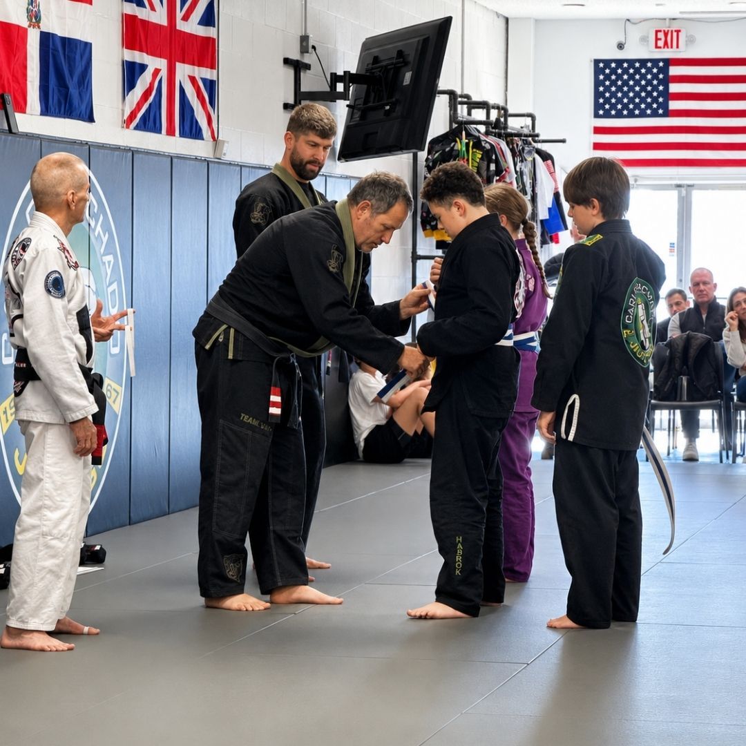 Two young children in blue and black martial arts uniforms grappling on a gym floor, one smiling.