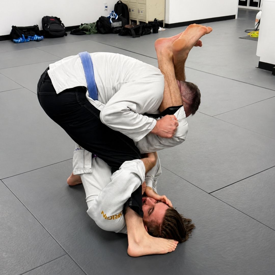 Two people practicing Brazilian Jiu-Jitsu on a mat. One is on top, applying a hold.