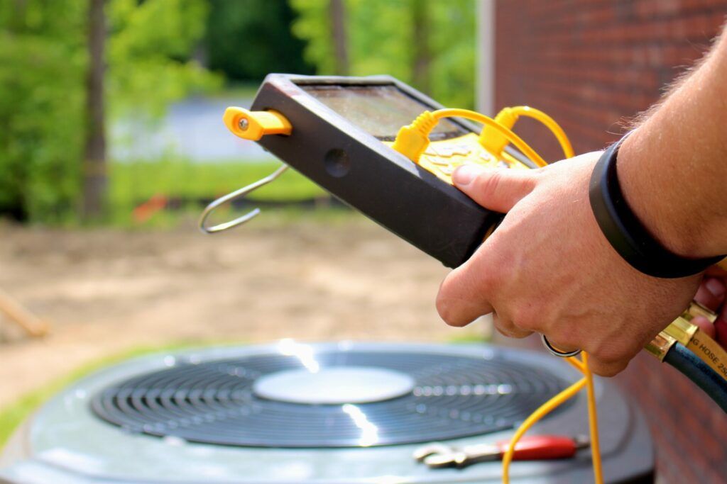 A person is holding a thermometer in front of an air conditioner.