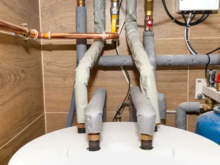 A close up of a water heater in a room with pipes.