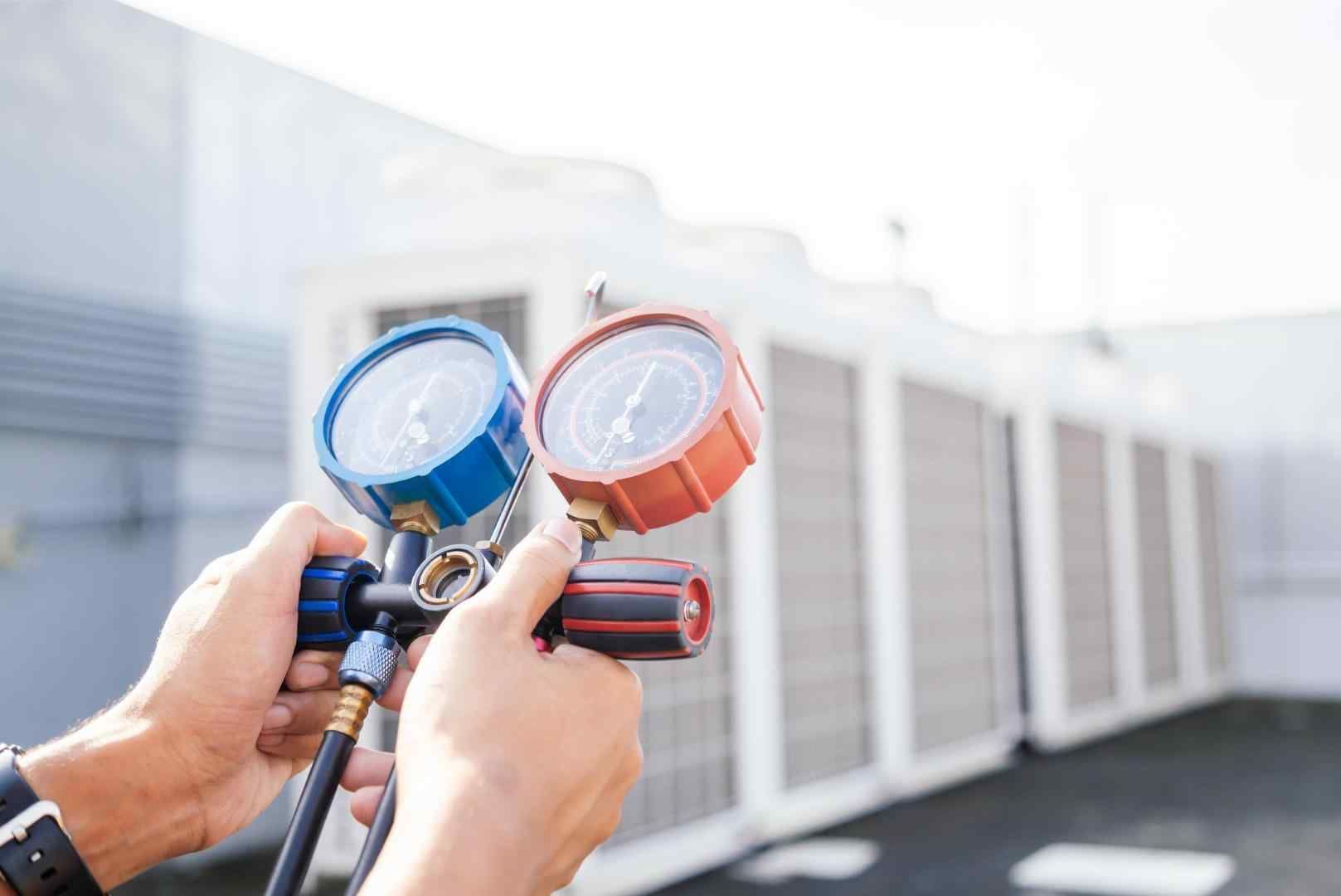 A person is holding two pressure gauges in their hands in front of a building.