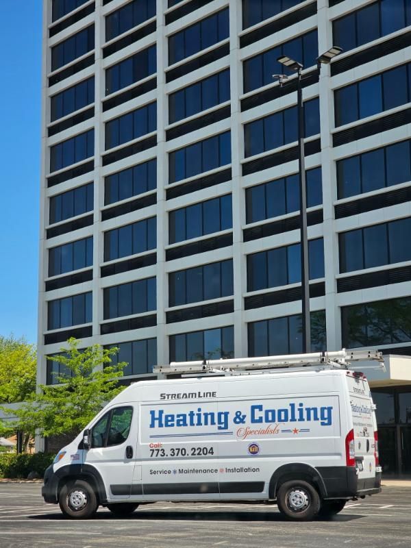 A heating and cooling van is parked in front of a tall building.