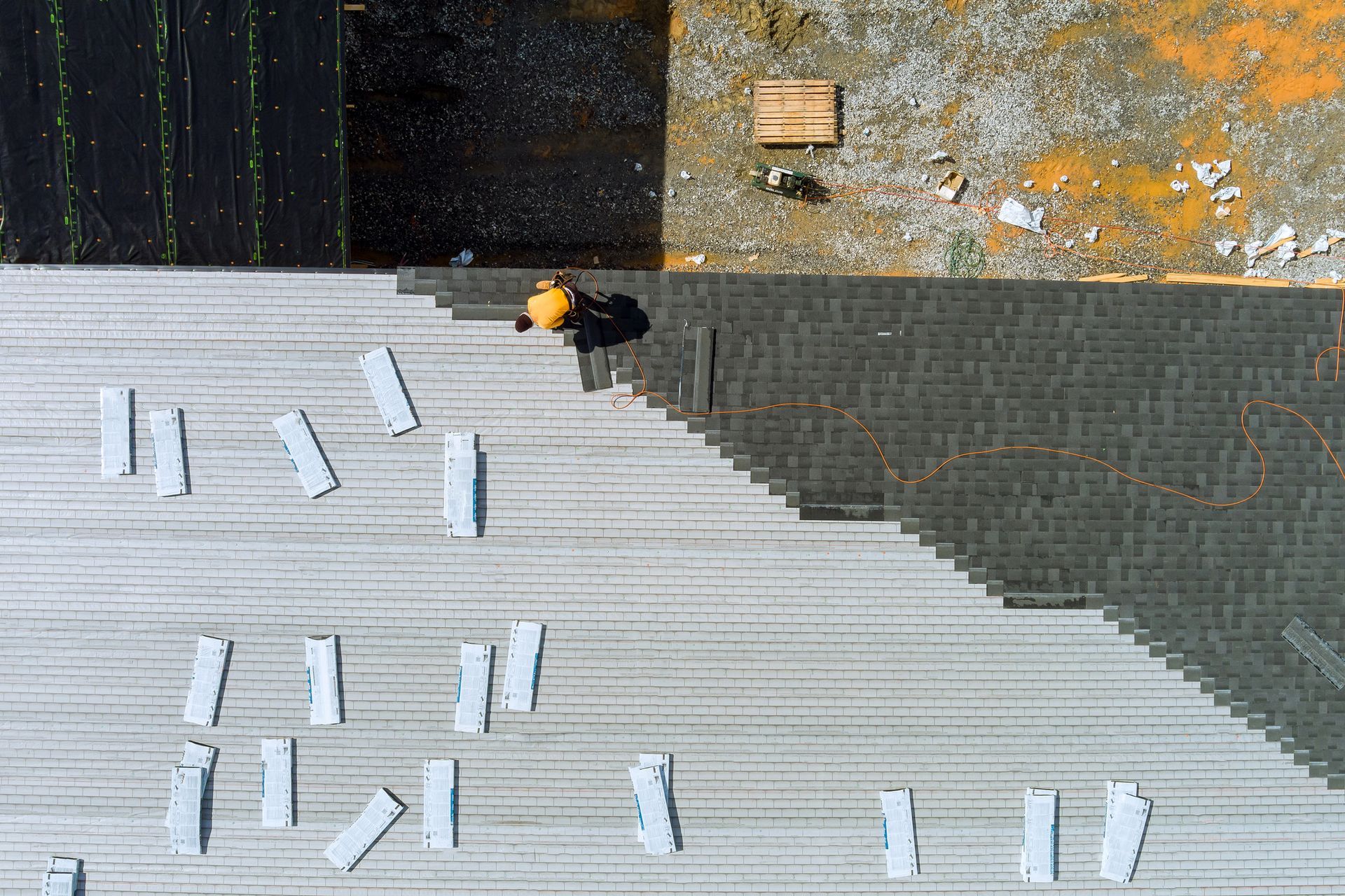 Roofer on a gray roof laying shingles, with a shadow and scattered materials.
