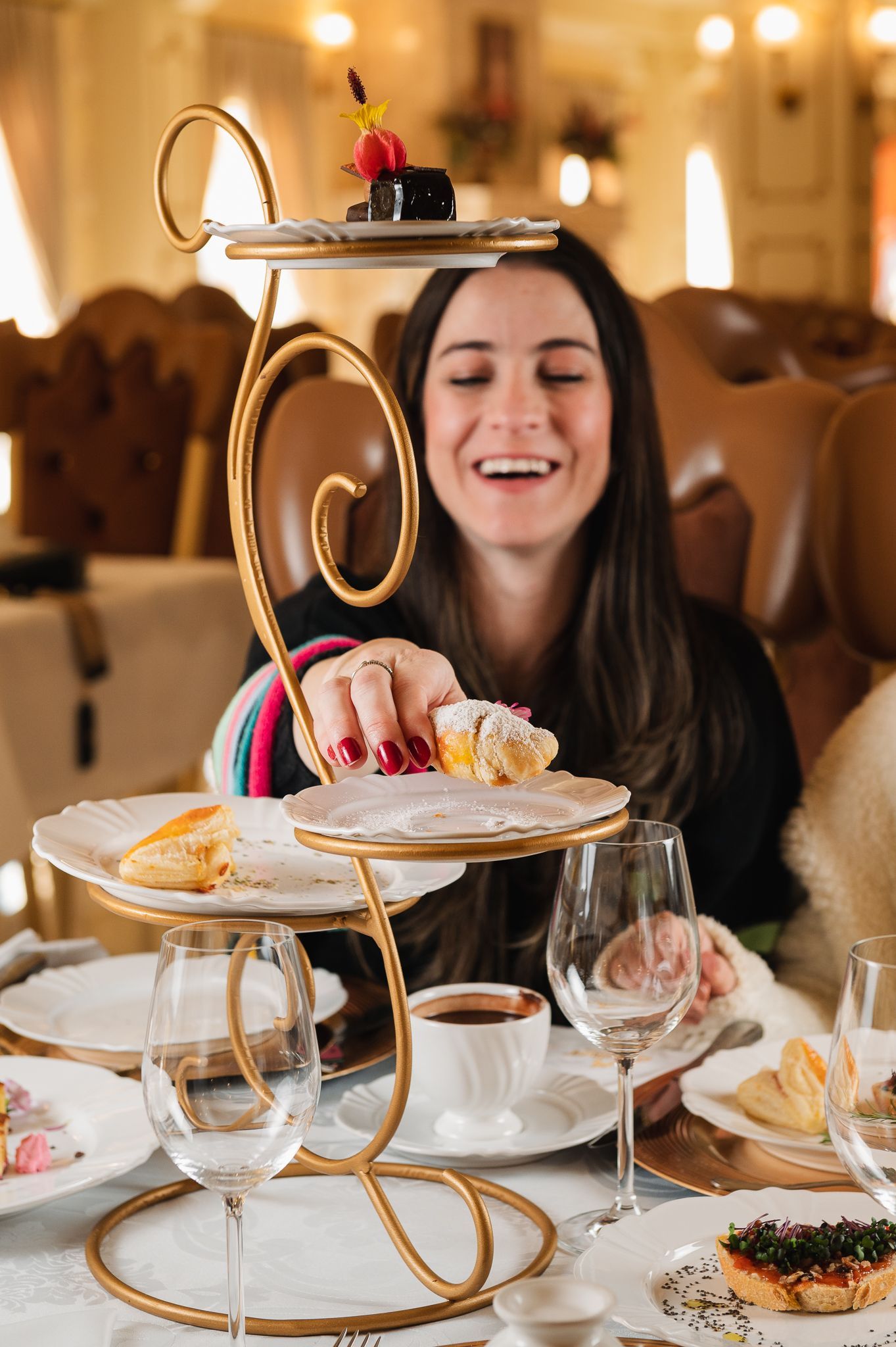 Uma mulher está sentada a uma mesa com pratos de comida e taças de vinho.