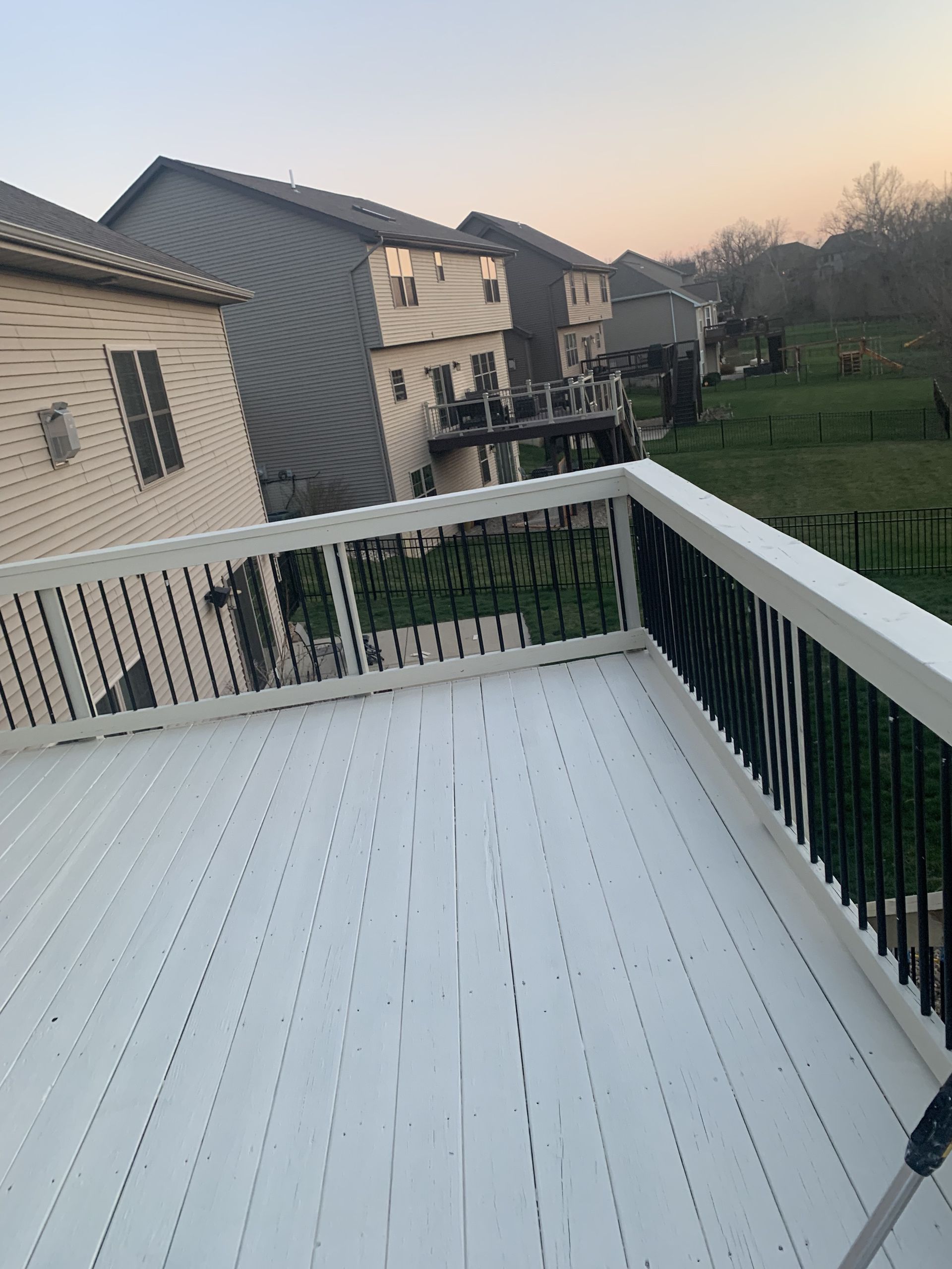 A white deck with a black railing and a house in the background