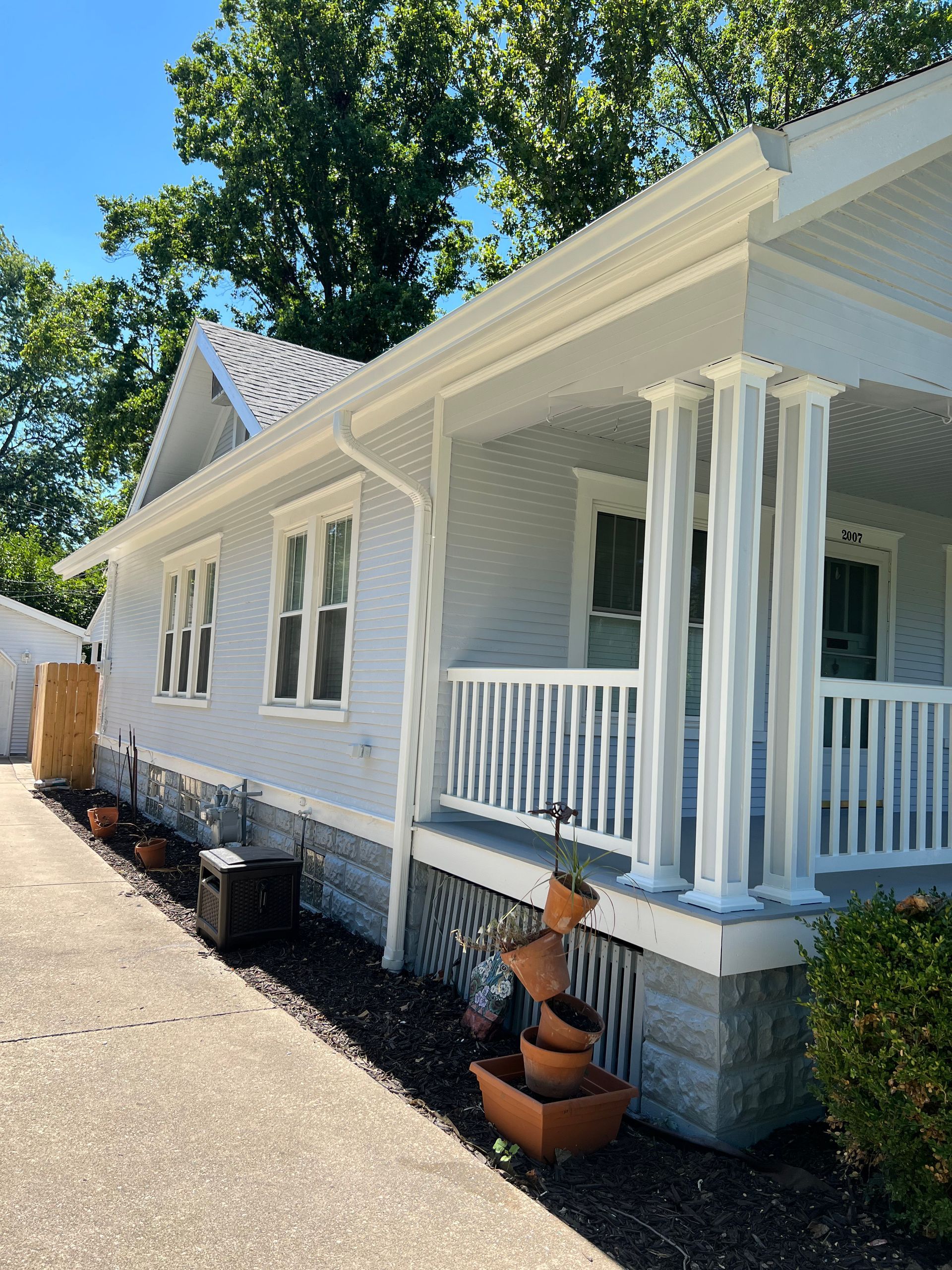 A white house with a porch and potted plants in front of it