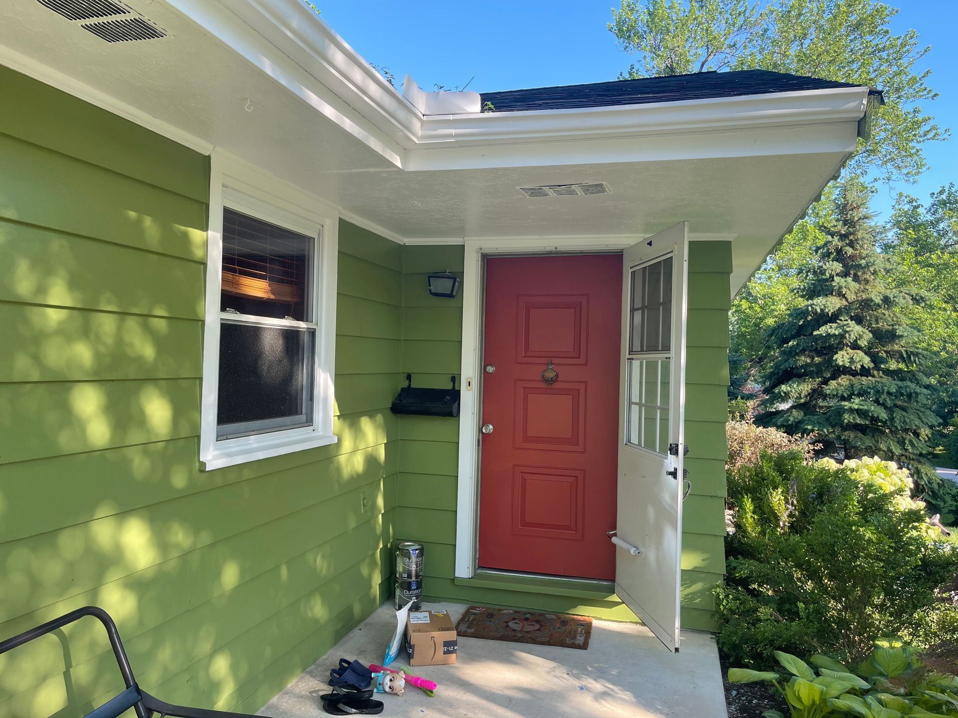 A green house with a red door and a white trim.