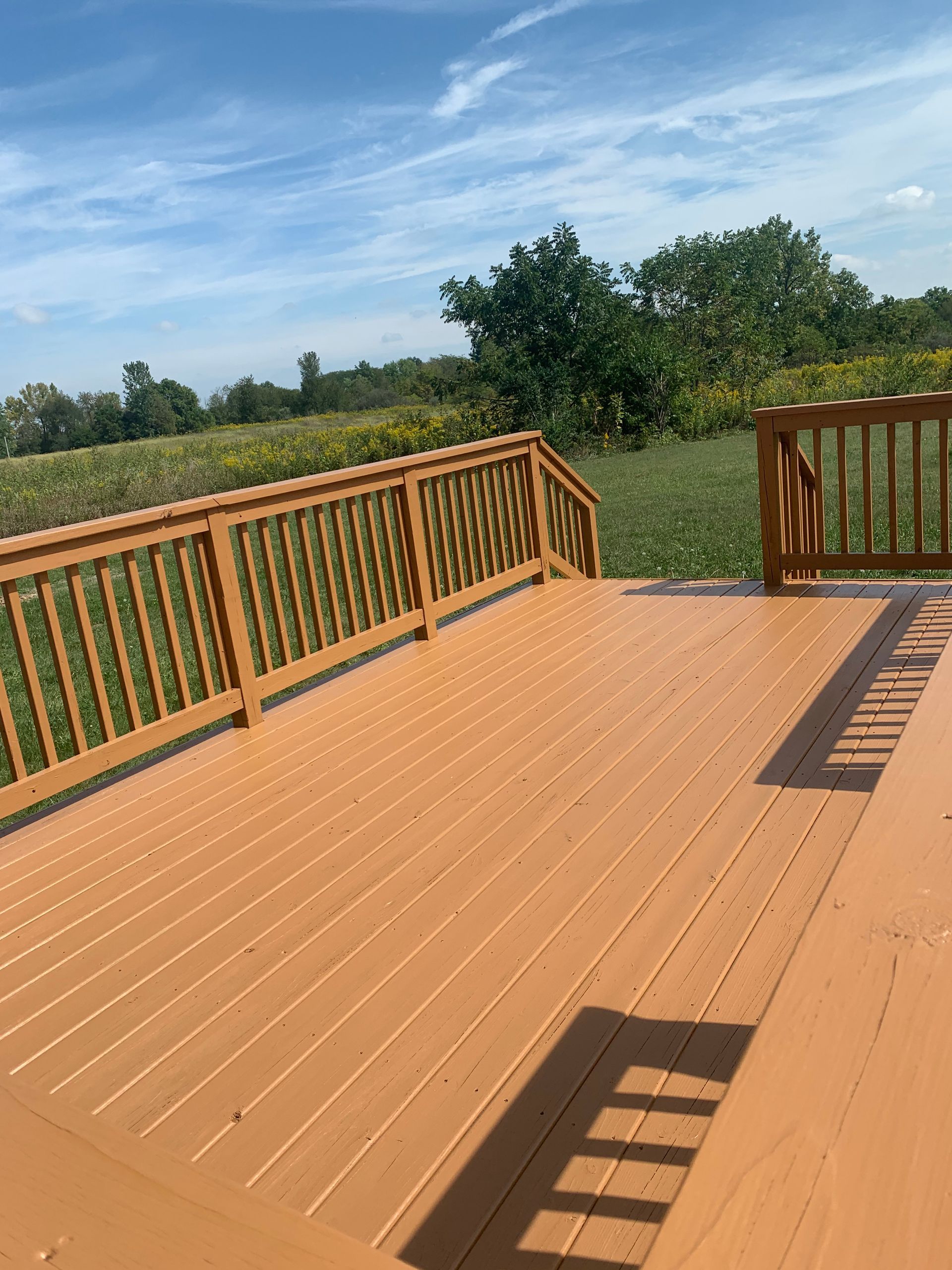 A wooden deck with a wooden railing and a view of a field.