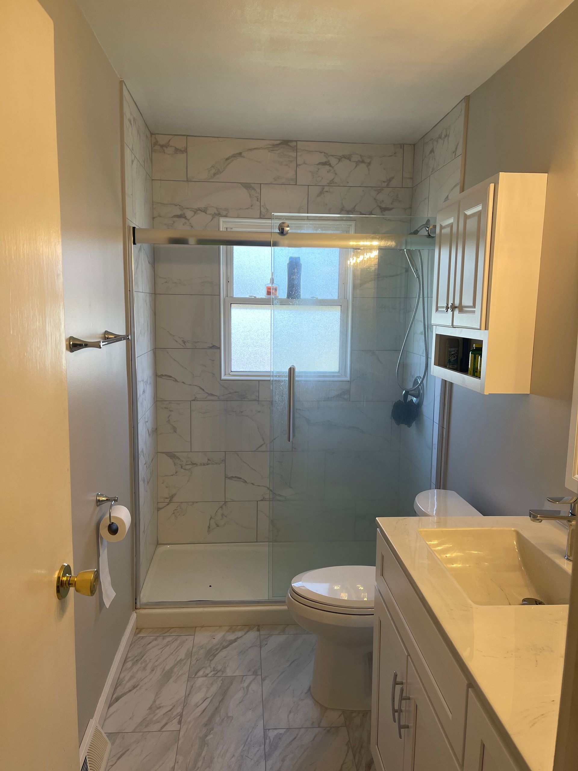 A bathroom with a toilet , sink , shower and window.