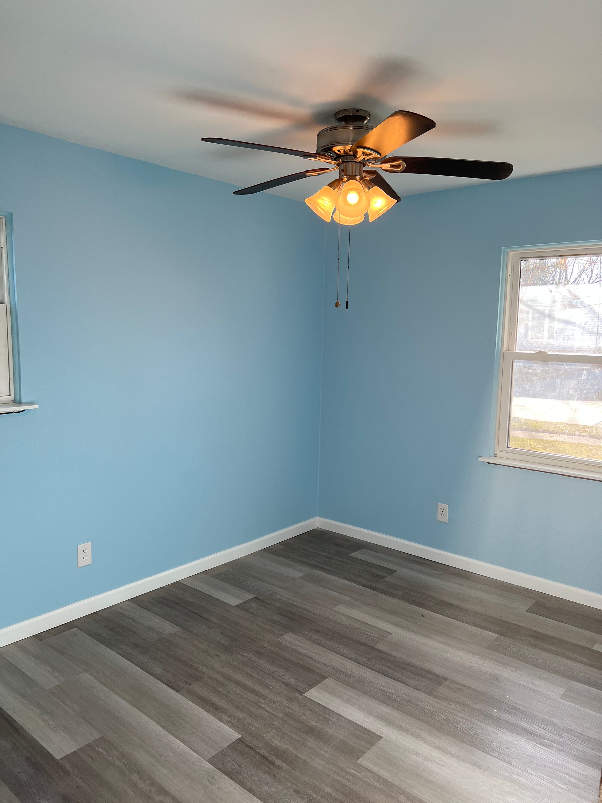 An empty room with blue walls and a ceiling fan.