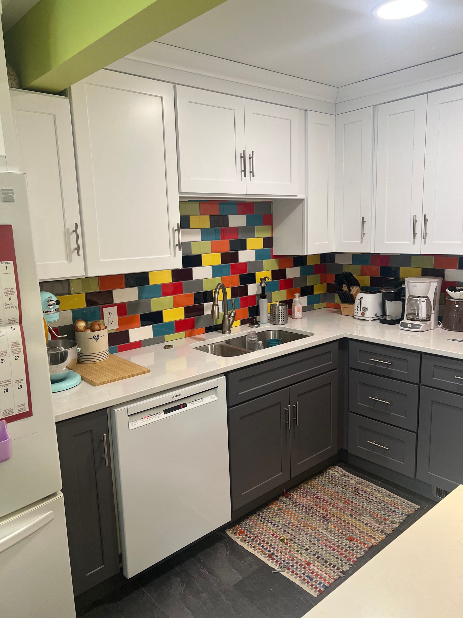 A kitchen with gray cabinets , white cabinets , a dishwasher , a sink , and a rug.
