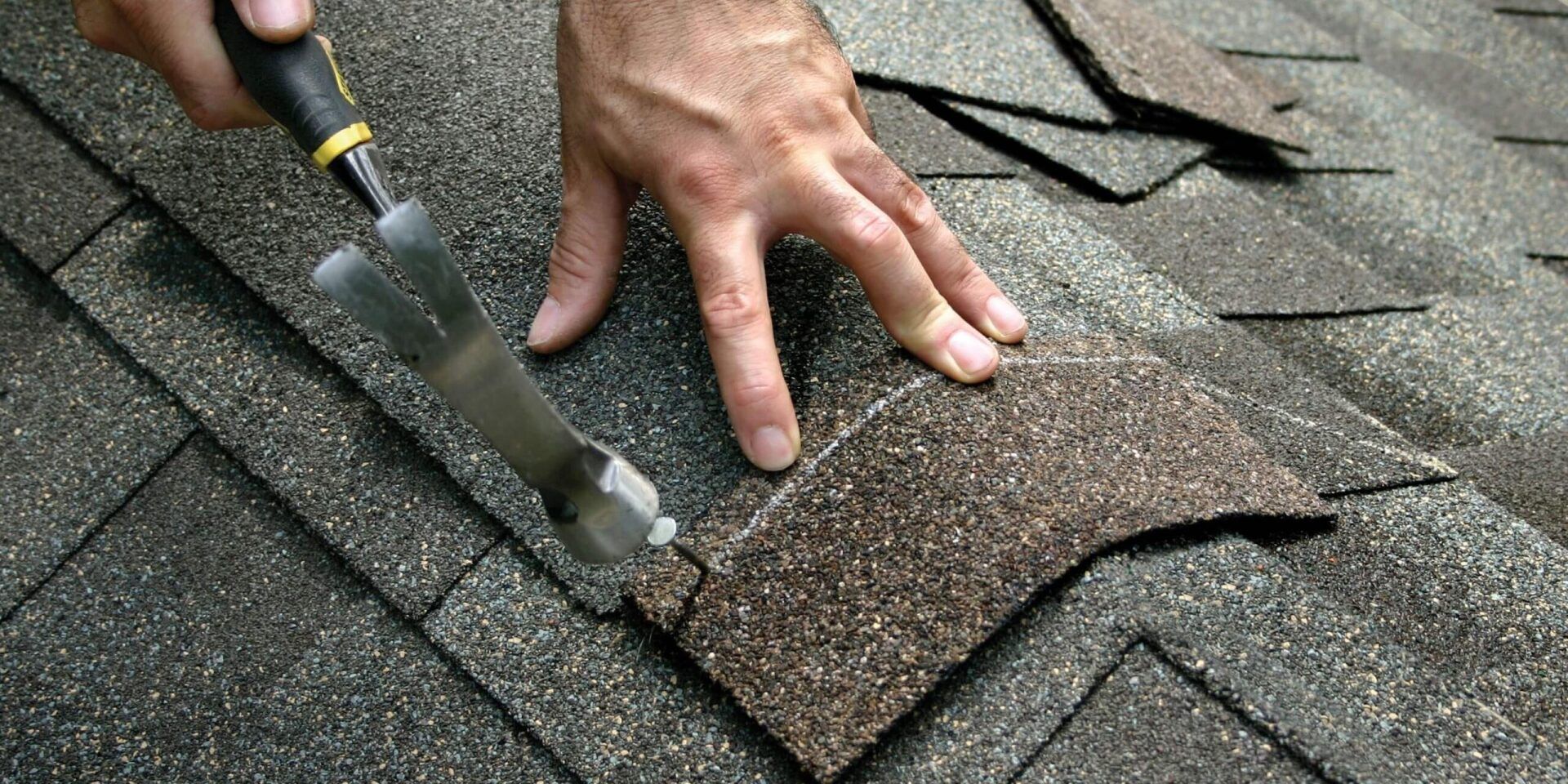 A person is using a hammer to remove shingles from a roof.