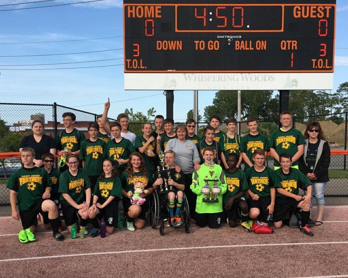 A group of people posing in front of a scoreboard that says home 0 guest 3